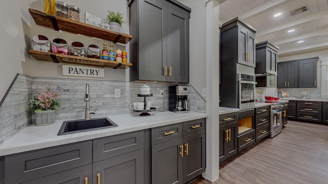 kitchen with sink, gray cabinets, appliances with stainless steel finishes, beamed ceiling, and light wood-type flooring