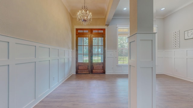 foyer with ornamental molding, a notable chandelier, light wood-type flooring, and french doors