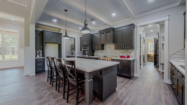 kitchen featuring hanging light fixtures, beam ceiling, an island with sink, and stainless steel oven