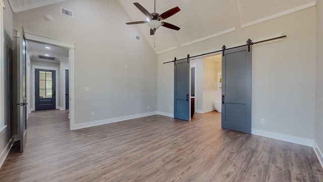 unfurnished bedroom featuring ceiling fan, hardwood / wood-style floors, high vaulted ceiling, ensuite bathroom, and a barn door