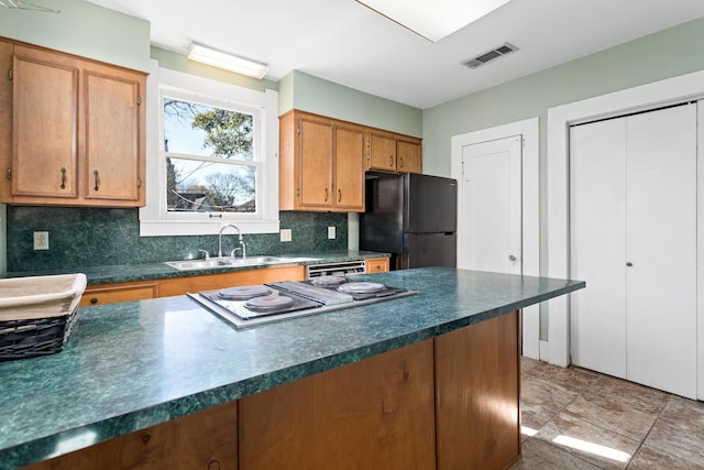 kitchen featuring black refrigerator, sink, backsplash, and stainless steel gas stovetop