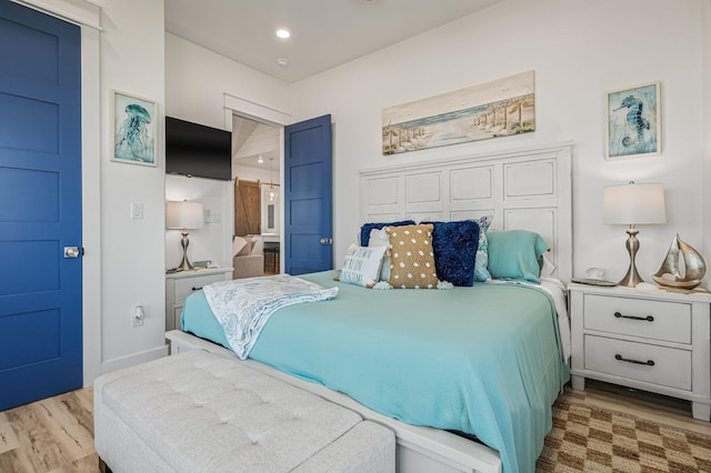 bedroom with a barn door and light wood-type flooring