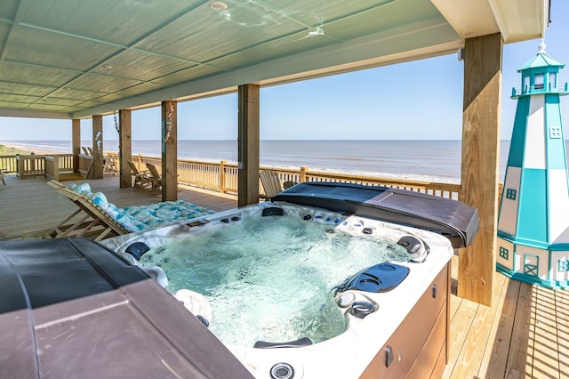 deck with a water view, a view of the beach, and a hot tub