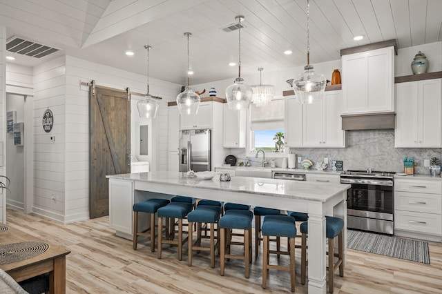 kitchen featuring a barn door, a kitchen island, stainless steel appliances, and decorative light fixtures