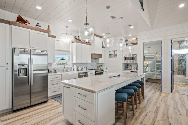 kitchen featuring light stone countertops, white cabinetry, a center island, hanging light fixtures, and appliances with stainless steel finishes