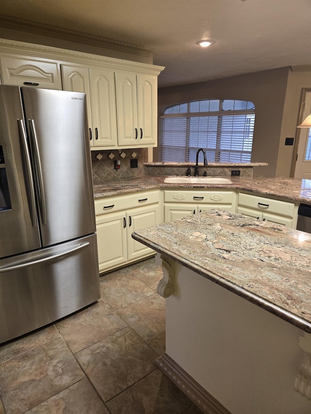 kitchen featuring white cabinetry, sink, light stone countertops, stainless steel fridge, and decorative backsplash