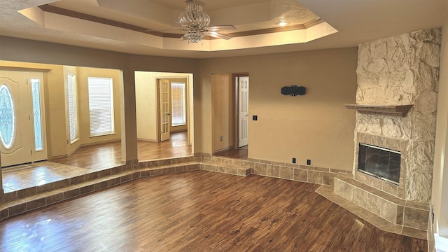 unfurnished living room featuring ceiling fan, a raised ceiling, wood-type flooring, and a tiled fireplace