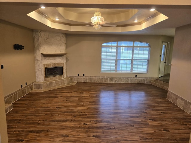 unfurnished living room featuring a chandelier, a tray ceiling, a stone fireplace, and dark hardwood / wood-style floors