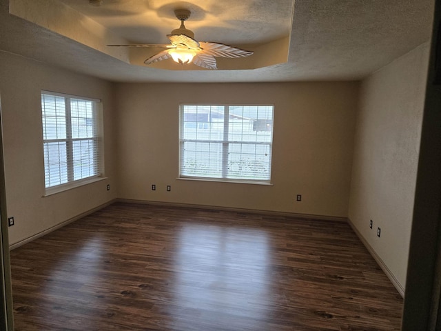 empty room with a raised ceiling, ceiling fan, dark hardwood / wood-style flooring, and a textured ceiling