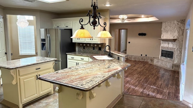 kitchen with pendant lighting, a center island, ceiling fan with notable chandelier, sink, and stainless steel fridge