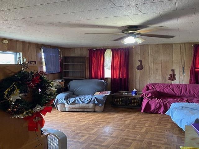 living room with ceiling fan, parquet floors, and wood walls