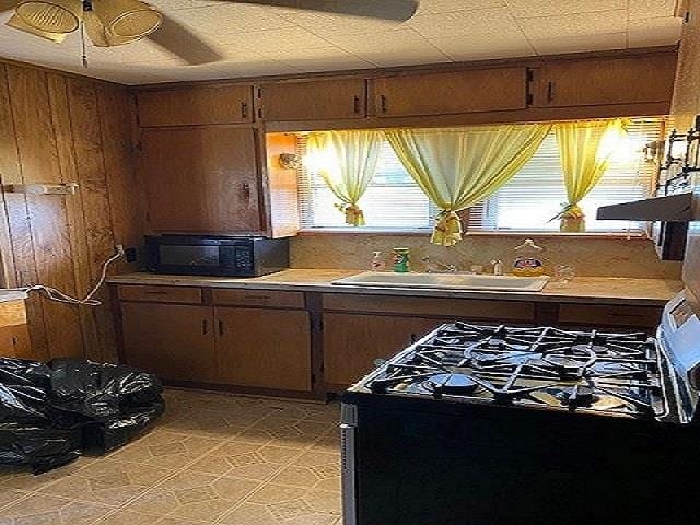 kitchen featuring black range with gas stovetop, sink, ceiling fan, and wood walls