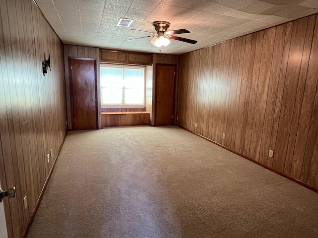 carpeted empty room with ceiling fan and wood walls