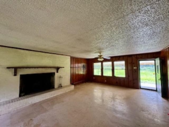 unfurnished living room with a textured ceiling, concrete floors, a ceiling fan, wood walls, and a brick fireplace