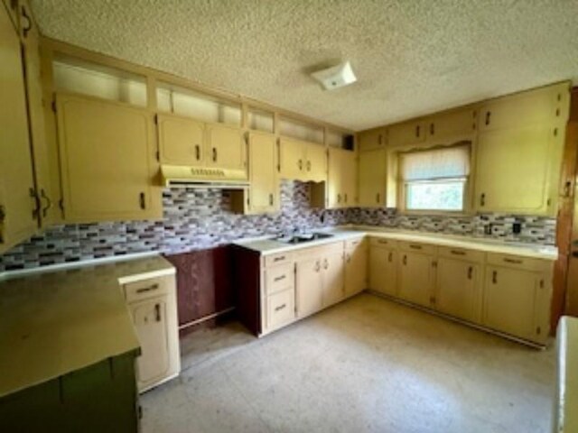 kitchen featuring light countertops, a textured ceiling, under cabinet range hood, backsplash, and light floors