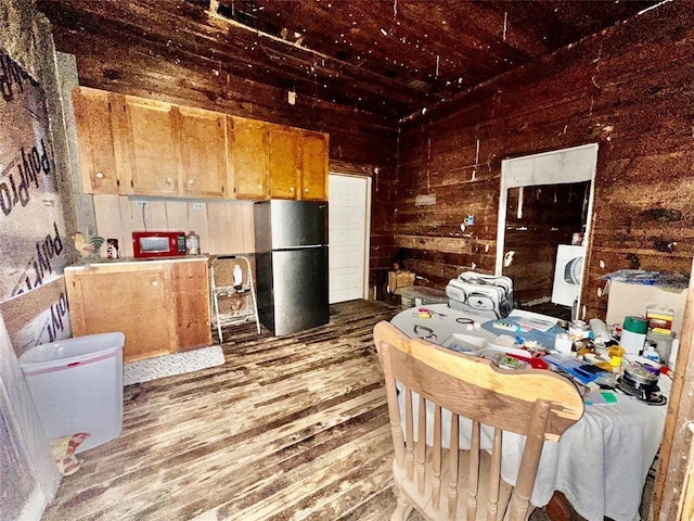 kitchen featuring stainless steel fridge, wooden walls, hardwood / wood-style floors, and washer / dryer