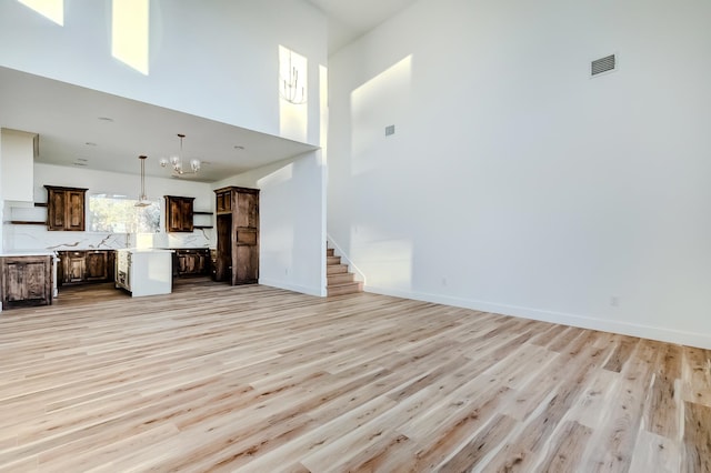 unfurnished living room featuring light hardwood / wood-style flooring, a towering ceiling, and a chandelier