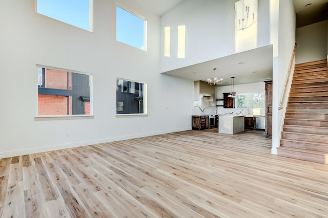 unfurnished living room with a notable chandelier, light wood-type flooring, and a high ceiling