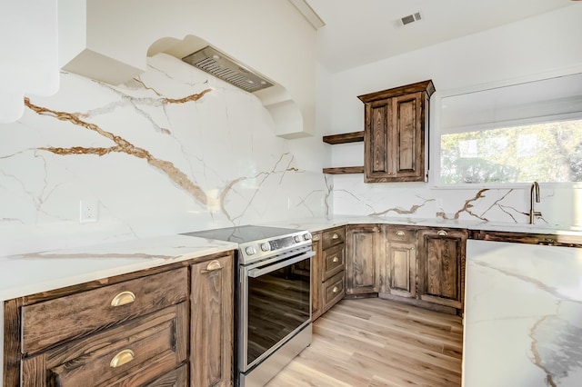 kitchen with light stone countertops, decorative backsplash, light hardwood / wood-style flooring, and stainless steel range with electric cooktop