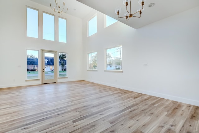 unfurnished living room with a high ceiling, light hardwood / wood-style floors, and a notable chandelier