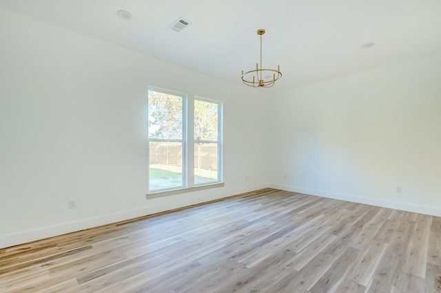 empty room featuring a chandelier and light hardwood / wood-style floors