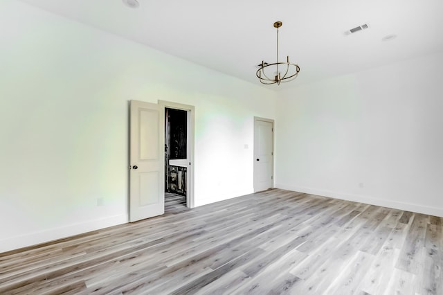 spare room with light wood-type flooring and an inviting chandelier