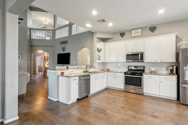 kitchen with light stone countertops, white cabinetry, stainless steel appliances, tasteful backsplash, and kitchen peninsula