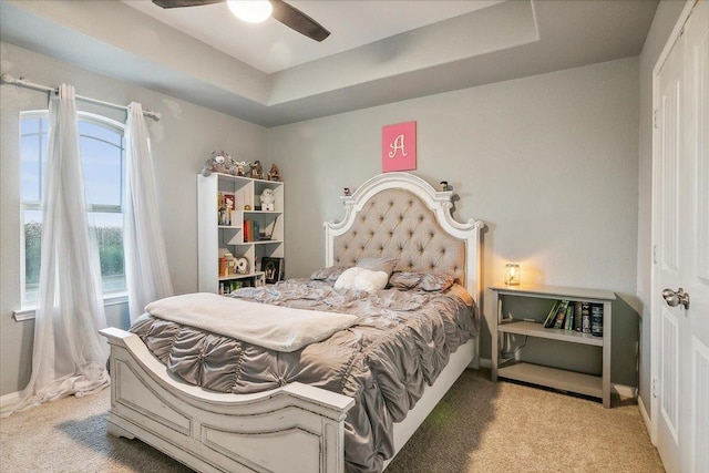 carpeted bedroom featuring ceiling fan and a tray ceiling