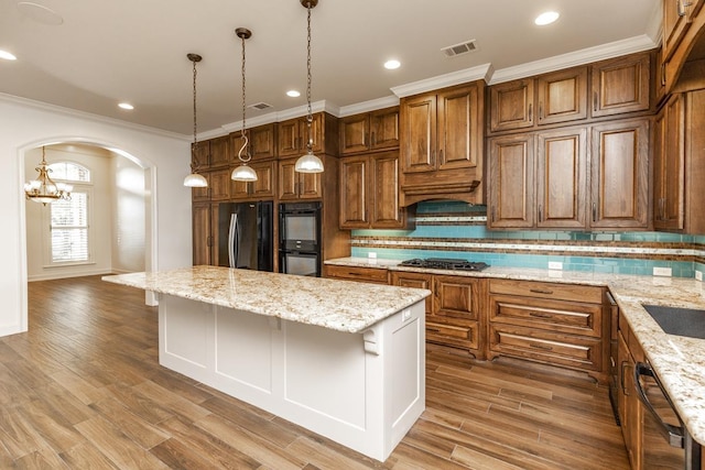 kitchen with a breakfast bar, hanging light fixtures, light stone counters, black appliances, and a kitchen island