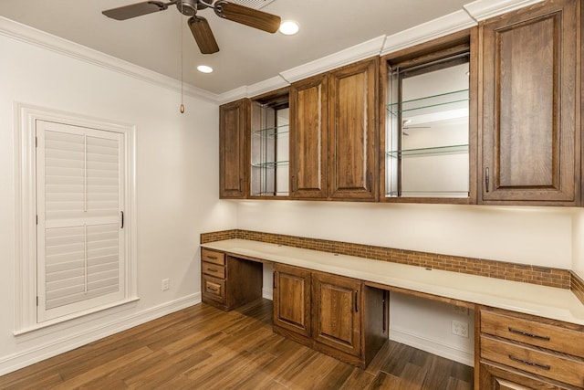 unfurnished office featuring ornamental molding, dark wood-type flooring, built in desk, and ceiling fan