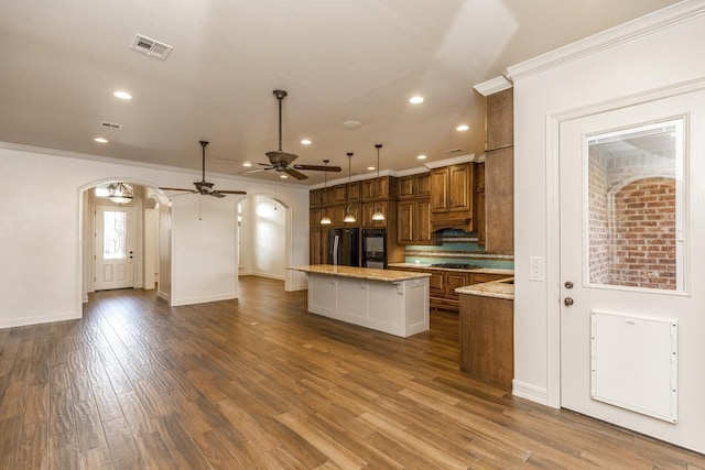 kitchen with gas stovetop, refrigerator, a kitchen island, pendant lighting, and light stone countertops