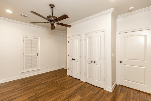 unfurnished bedroom featuring multiple closets, ceiling fan, dark hardwood / wood-style floors, and crown molding