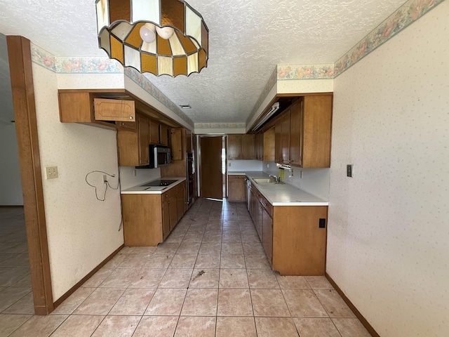 kitchen with black electric cooktop, a textured ceiling, stainless steel microwave, wallpapered walls, and light countertops