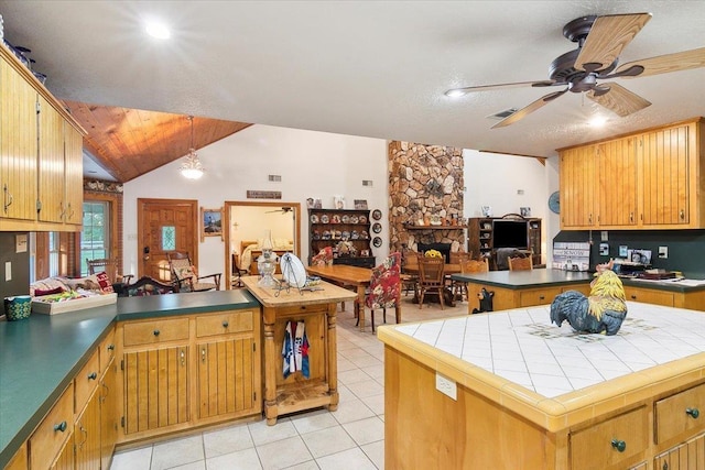 kitchen featuring light tile patterned flooring, vaulted ceiling, a fireplace, a kitchen island, and kitchen peninsula