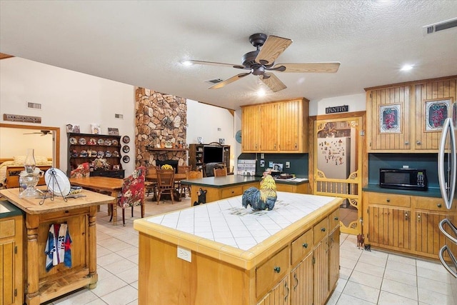 kitchen featuring a center island, a stone fireplace, light tile patterned floors, a textured ceiling, and tile counters