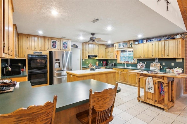 kitchen featuring light tile patterned floors, a textured ceiling, double oven, a kitchen island, and stainless steel fridge with ice dispenser