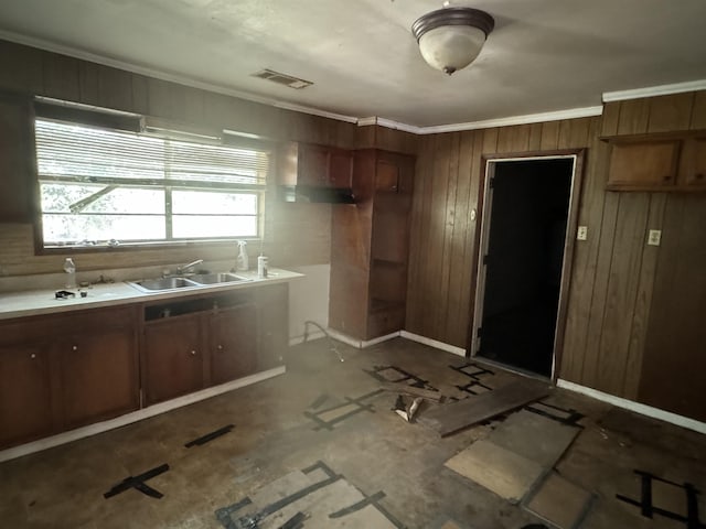 kitchen with baseboards, visible vents, ornamental molding, wood walls, and a sink