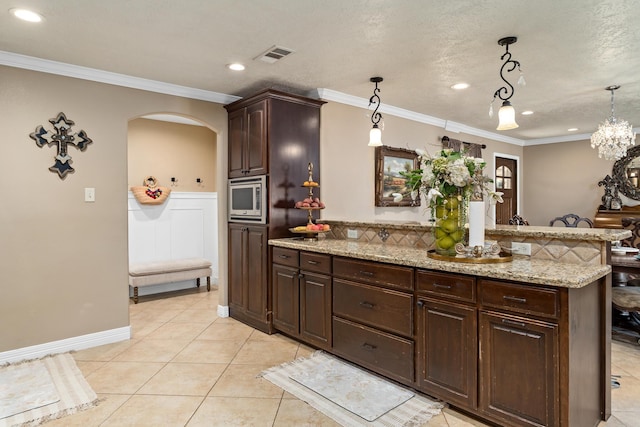 134 Hornbeam, Village Mills, TX 77663 - kitchen featuring stainless steel microwave, arched walkways, light tile patterned floors, dark brown cabinetry, and hanging light fixtures
