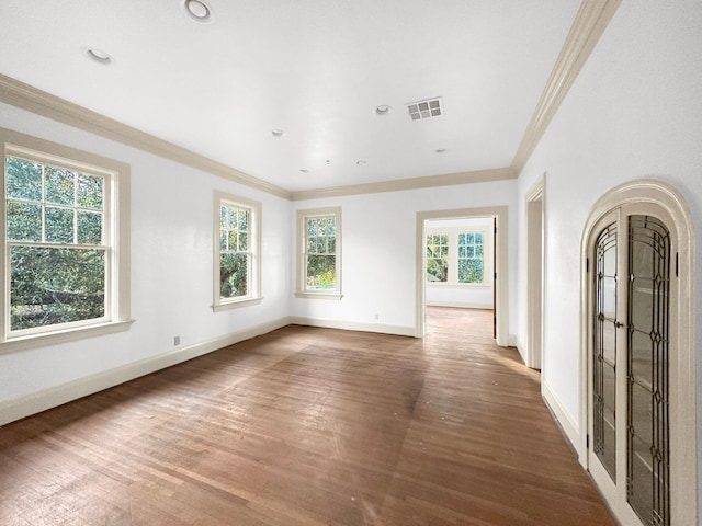 empty room with visible vents, baseboards, crown molding, and wood finished floors