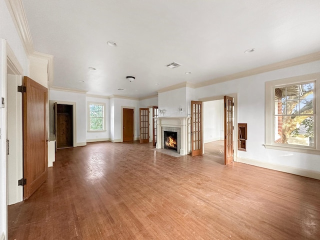 unfurnished living room with visible vents, ornamental molding, light wood-type flooring, baseboards, and a tile fireplace