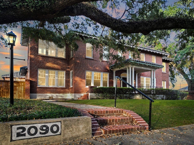 view of front of house featuring a yard, fence, and brick siding