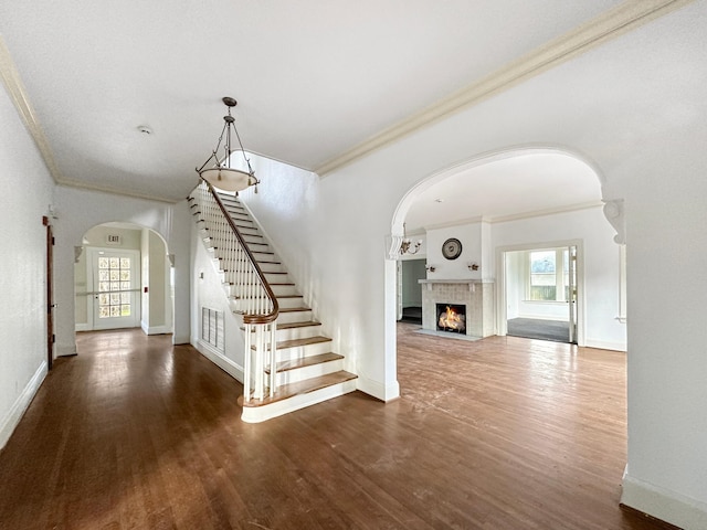 foyer entrance featuring arched walkways, a fireplace with flush hearth, stairway, ornamental molding, and wood finished floors