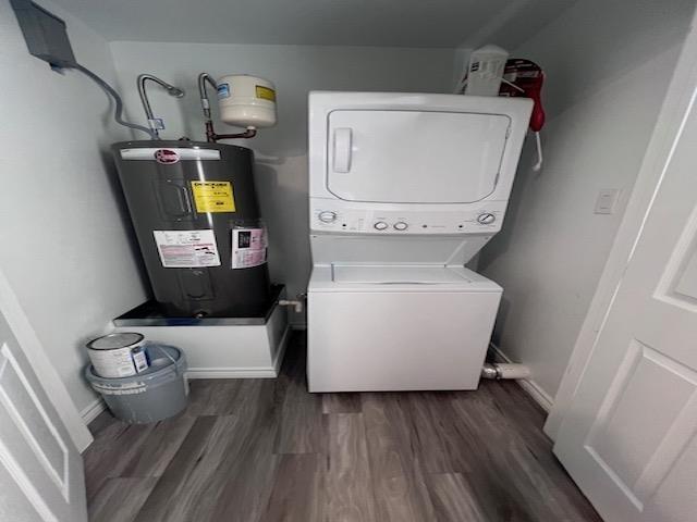 laundry area featuring electric water heater, dark hardwood / wood-style flooring, and stacked washer / drying machine