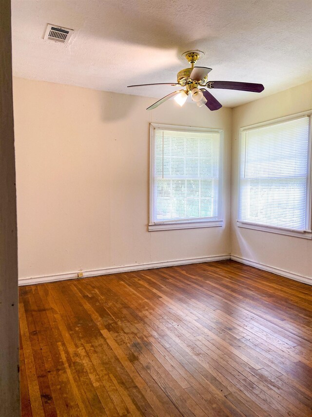 empty room featuring ceiling fan, plenty of natural light, dark wood-type flooring, and a textured ceiling