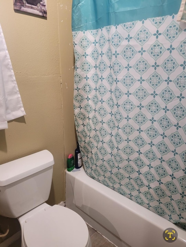 full bathroom featuring a textured wall, shower / bath combo, and toilet