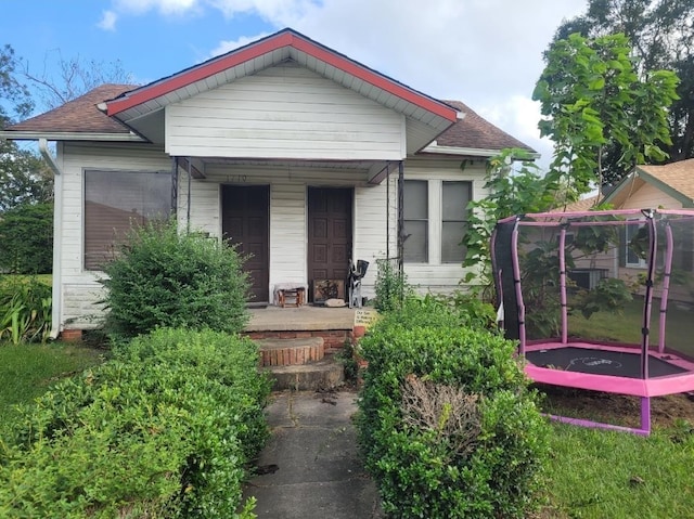 bungalow featuring a porch, a trampoline, and a shingled roof