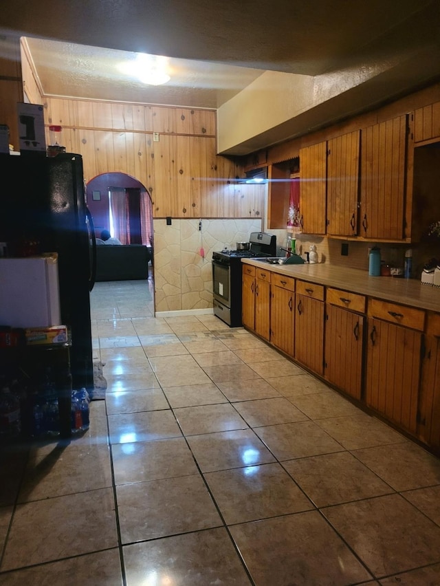 kitchen with light tile patterned floors, gas range, freestanding refrigerator, light countertops, and a sink