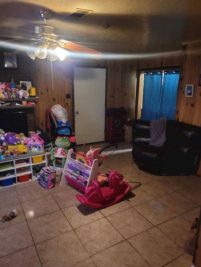 game room featuring a textured ceiling, wood walls, a ceiling fan, visible vents, and tile patterned floors