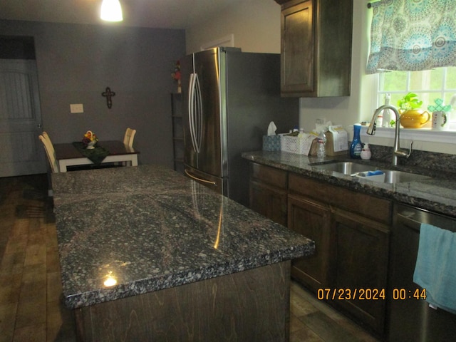 kitchen featuring dark stone counters, a center island with sink, sink, appliances with stainless steel finishes, and dark brown cabinetry