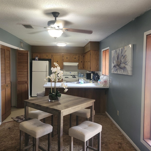 kitchen with white appliances, kitchen peninsula, ceiling fan, and carpet